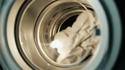 White Fabric Tumbles Inside A Spinning Washing Machine Drum