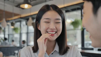 Young Asian Woman Laughing During Conversation In Cafe