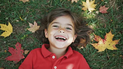 Happy Young Child Laughing While Lying On Autumn Leaves