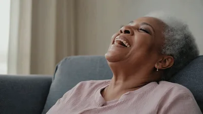 Happy Senior Woman Laughing While Sitting On Sofa