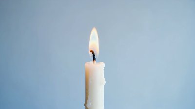 Single White Candle Burning Against A Plain Background