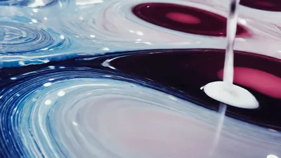 White Liquid Pouring Into Colorful Swirling Paint Surface