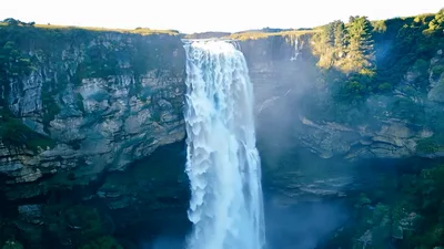 Aerial View Of Cascading Waterfall In Lush Green Canyon