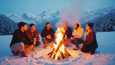 Friends Sitting Around A Campfire In Snowy Mountains