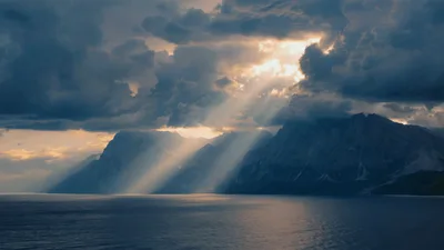 Sunlight Beams Shining Through Dark Clouds Over Mountains