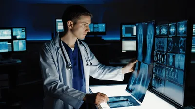Doctor Examining Medical X-Ray Scans In Dark Hospital Office