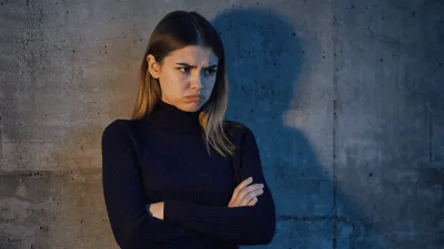 Upset Young Woman Standing Against Concrete Wall