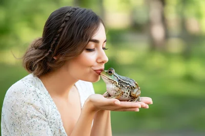 Young Woman Kissing A Frog In A Park