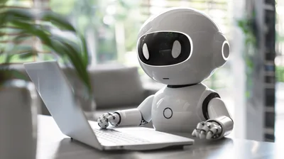 Small White Robot Typing On A Laptop