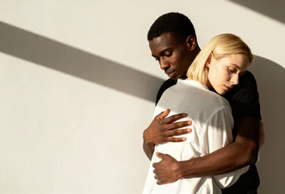 Interracial Couple Embracing Against A Minimalist Wall