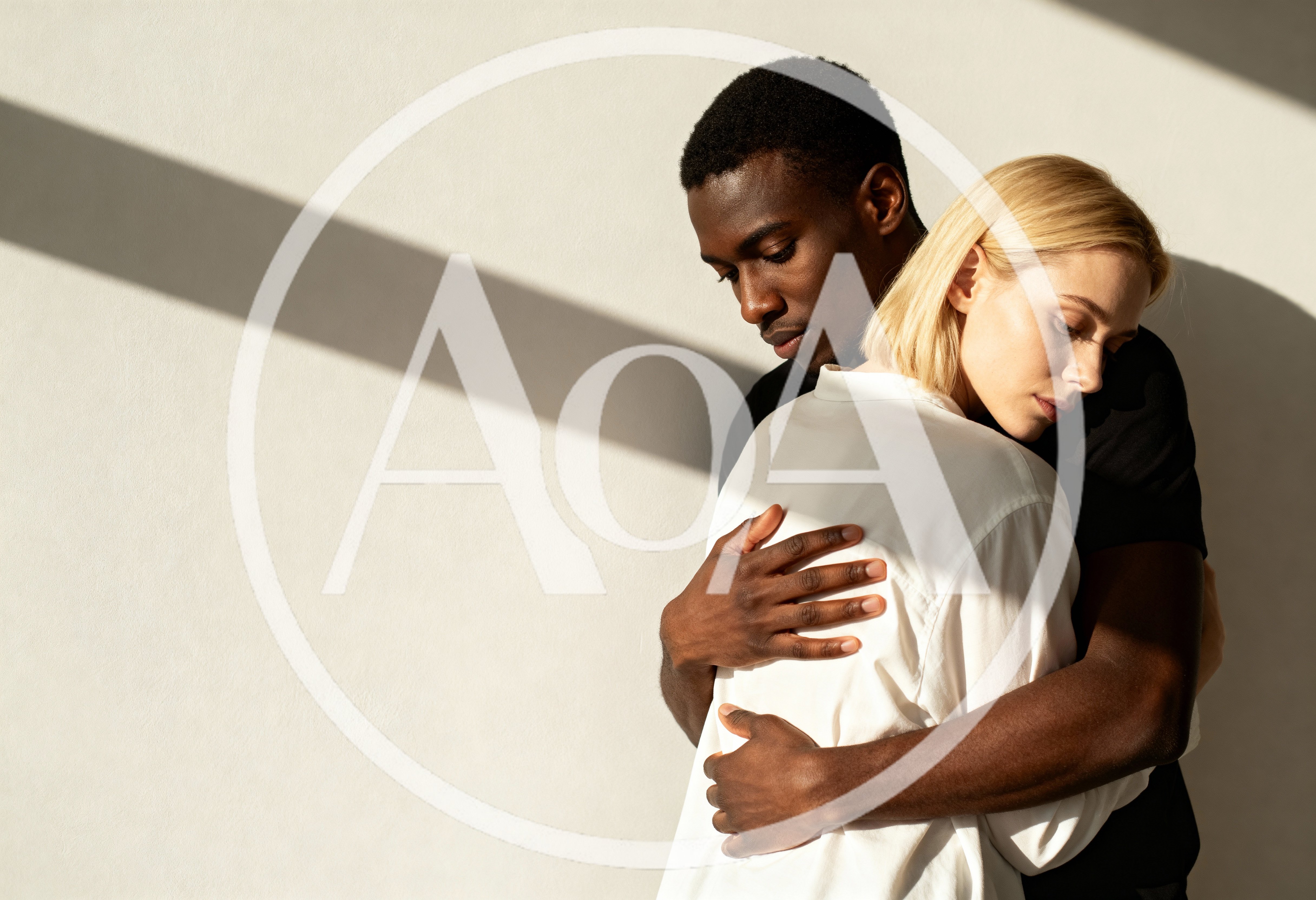 Interracial Couple Embracing Against A Minimalist Wall