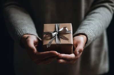 Person Holding A Small Gift Wrapped In Brown Paper