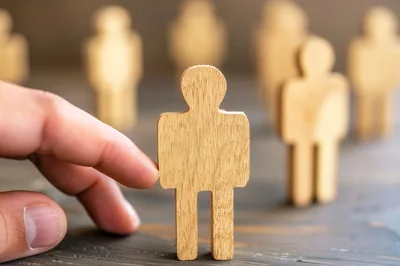Hand Selecting A Wooden Human Figure From A Group