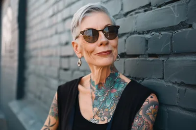 Stylish Older Woman With Tattoos Leaning Against Brick Wall