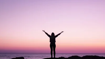 Woman Standing With Arms Raised At Sunset
