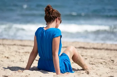 Young Woman Sitting On Sandy Beach In Blue Dress