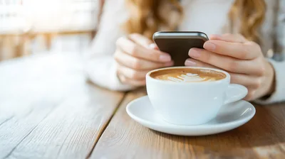 Woman Using Smartphone While Drinking Coffee In Cafe