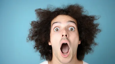 Surprised Young Man With Curly Hair Looking At Camera