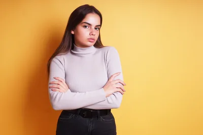 Young Woman With Crossed Arms Posing Against Yellow Background