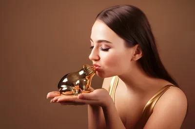 Young Woman Kissing A Golden Frog Figurine