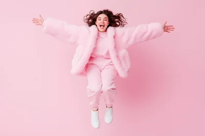 Happy Young Woman Jumping in Pink Fur Coat