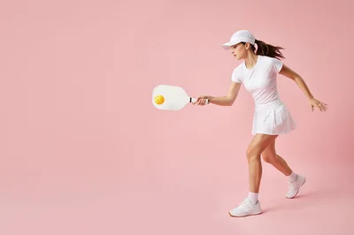 Young Woman Playing Pickleball on Pink Background
