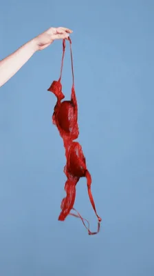 Hand Dropping Red Lace Bra Against Blue Background