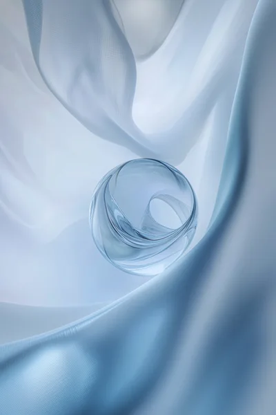 Abstract Glass Sphere Floating Above Flowing Blue Fabric