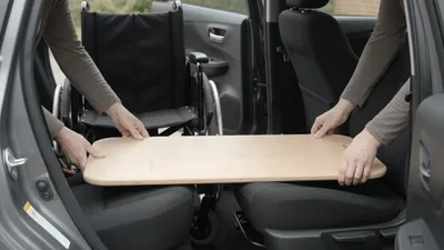 Caregiver Using Transfer Board To Move Patient Into Car