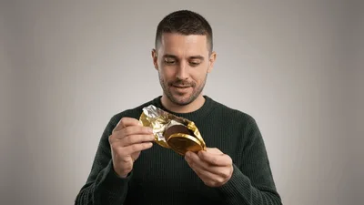 Man Unwrapping A Chocolate Coin And Looking Disappointed