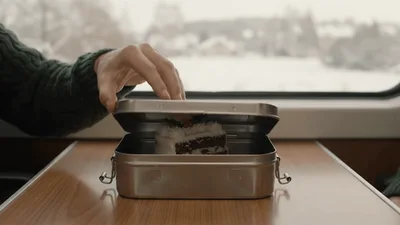 Two People Opening A Metal Lunchbox With Christmas Cake