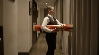 Waitress Carrying Large Christmas Cracker Through Hotel Hallway