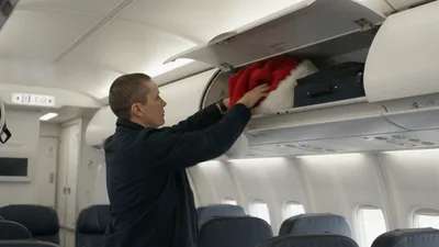 Flight Attendant Stowing Santa Hat In Overhead Bin