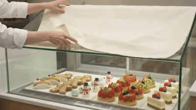Baker Uncovering Fresh Pastries In A Glass Display Case