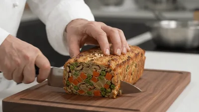 Chef Slicing Vegetable Nut Loaf On Wooden Board