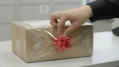 Hand Removing Red Decorative Bow From Cardboard Parcel