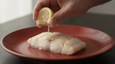 Hand Squeezing Fresh Lemon Juice Over Raw Cod Fillet