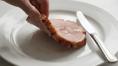 Hand Lifting A Slice Of Glazed Ham