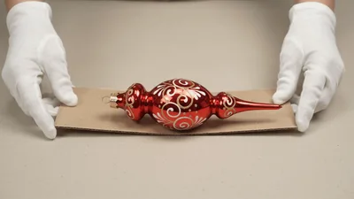 Hands Placing Red Christmas Ornament On Cardboard Base