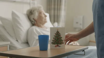 Nurse Placing Christmas Card On Hospital Bedside Table