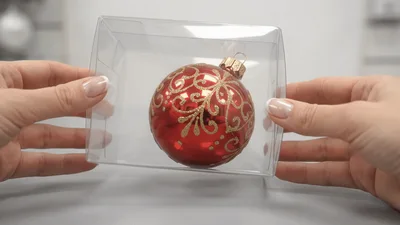 Hands Holding A Red Christmas Ornament In Clear Box