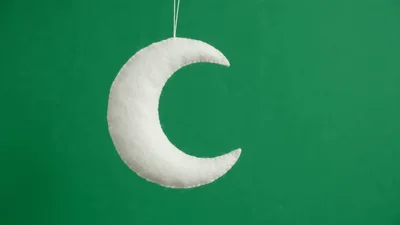 White Felt Crescent Moon Hanging Against Green Background