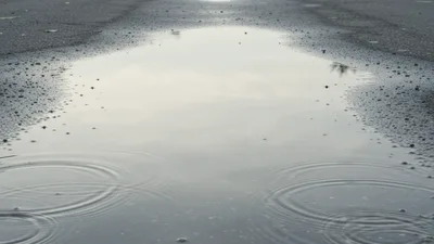 Raindrops Falling Into A Puddle On Asphalt