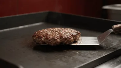Chef Flipping A Beef Burger Patty On A Griddle