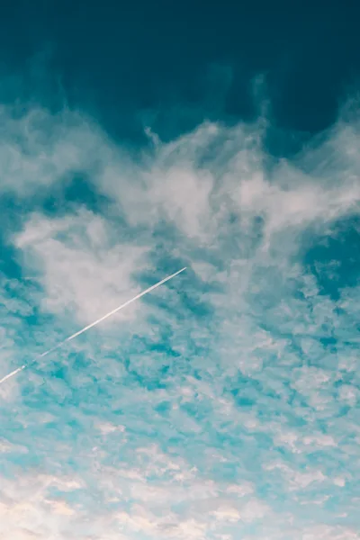 Airplane Contrail Across A Cloudy Blue Sky