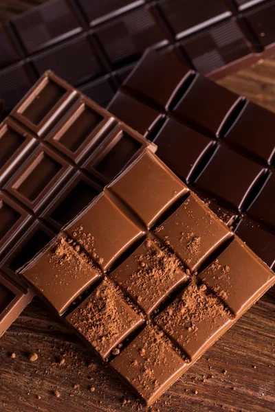 Assorted Chocolate Bars With Cocoa Powder On Wooden Surface