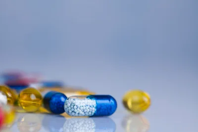 Blue And Yellow Medical Capsules On Reflective Surface