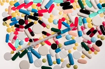 Assorted Pharmaceutical Pills and Syringe on White Background