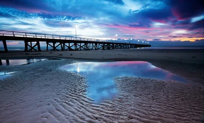 Wooden Pier Extending Over Sandy Beach At Sunset