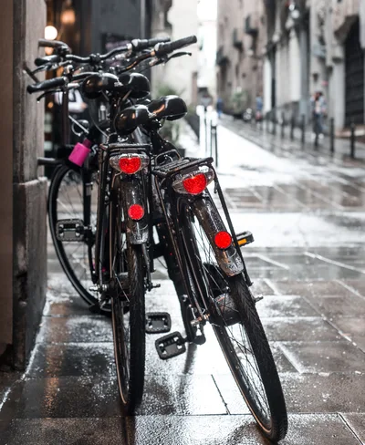 Two Black Bicycles Parked On A Wet City Street